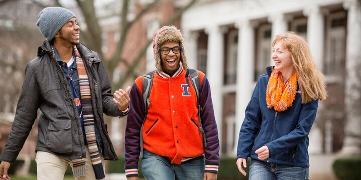 Three students walk on the sidewalk on the Main Quad with the English Building in background.