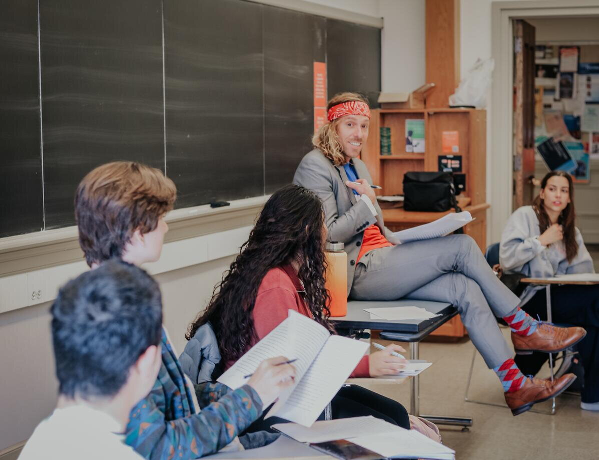 Teacher sitting on a table while teaching students