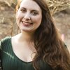 Rebecah is smiling directly at the camera. Her long brown hair is pulled to one side and she is wearing a forest green sweater.